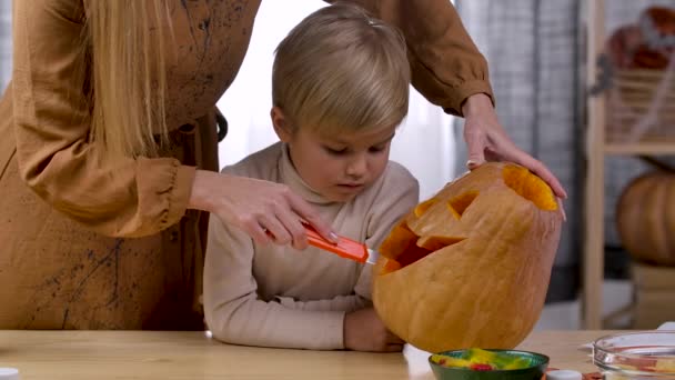 Mamma visar sin son hur man gör en Halloween Jack Lantern ansikte på den stora orange pumpa. Närbild av en kvinnlig hand rista ett hemskt ansikte på en pumpa. Långsamma rörelser. — Stockvideo