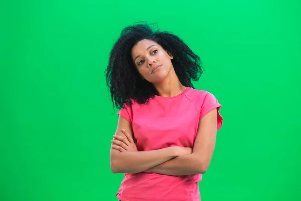 Portrett av unge kvinnelige afroamerikanere som tenker på noe, opprørt over at det ikke er noen anelse. En svart kvinne med krøllete hår i rosa skjorte poserer på en grønn skjerm i studioet. Lukk. – stockfoto