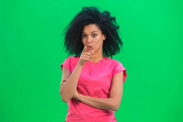 Portrett av unge kvinnelige afroamerikanere som peker på kameraet med pekefingeren din. En svart kvinne med krøllete hår i rosa skjorte poserer på en grønn skjerm i studioet. Lukk. – stockfoto