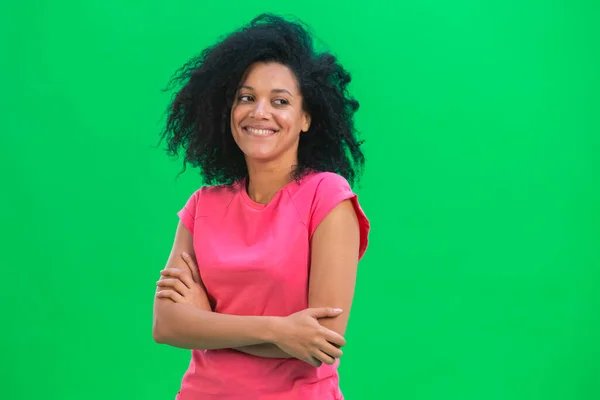 Portrett av unge kvinnelige afroamerikanske flørtete smil. En svart kvinne med krøllete hår i rosa skjorte poserer på en grønn skjerm i studioet. Lukk. – stockfoto