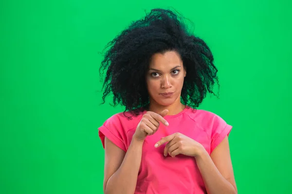 Portrett av unge afroamerikanere som er sinte og ser til siden. En svart kvinne med krøllete hår i rosa skjorte poserer på en grønn skjerm i studioet. Lukk. – stockfoto