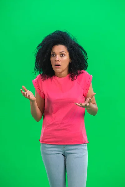 Portrett av en ung kvinnelig afrikansk-amerikansk sint og opprørt. En svart kvinne med krøllete hår i rosa skjorte poserer på en grønn skjerm i studioet. Lukk. – stockfoto