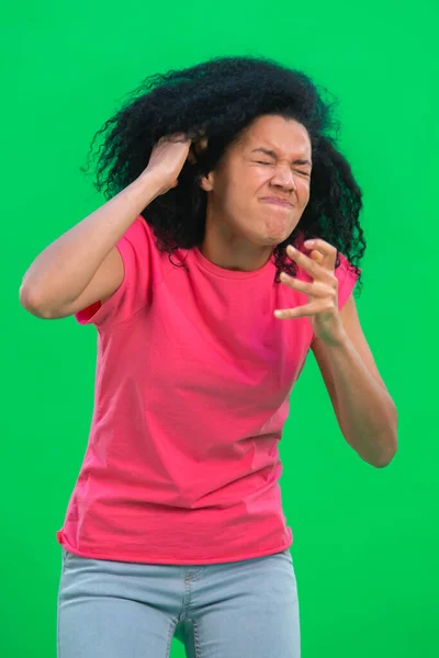 Retrato de una joven afroamericana enojada y muy molesta. Mujer negra con el pelo rizado en camiseta rosa posa en la pantalla verde en el estudio. De cerca.. —  Fotos de Stock