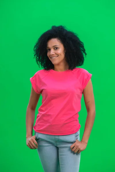 Portrett av unge kvinnelige afroamerikanere som smilte lykkelig. En svart kvinne med krøllete hår i rosa skjorte poserer på en grønn skjerm i studioet. Lukk. – stockfoto