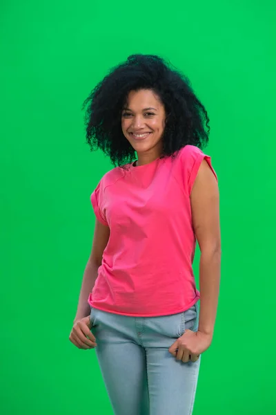 Portrett av unge kvinnelige afroamerikanere som smilte lykkelig. En svart kvinne med krøllete hår i rosa skjorte poserer på en grønn skjerm i studioet. Lukk. – stockfoto