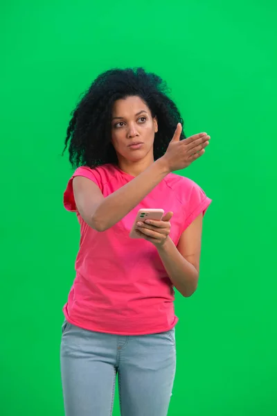 Portrait of young female African American viewing the map on a smartphone to get to the right place. Black woman with curly hair poses on green screen in the studio. Close up. — Stock Photo, Image