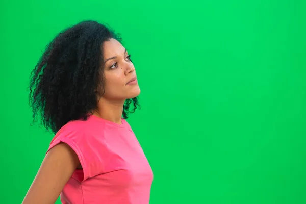 Nuoren afroamerikkalaisen naisen muotokuva harkitsee ja valitsee jotain. Musta nainen kihara tukka vaaleanpunainen t paita aiheuttaa vihreällä ruudulla studiossa. Sulje se.. — kuvapankkivalokuva