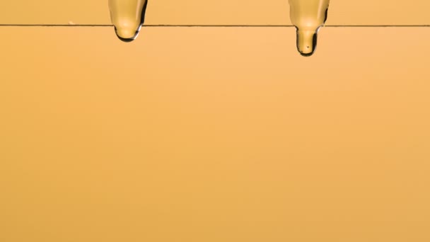 Makro záběr husté tekuté kapky medu tekoucí po skle a padající na hnědé pozadí studia s měkkým světlem. Zlatý sladký med kapající po sladké tekutině. Zavřít. Zpomalený pohyb. — Stock video