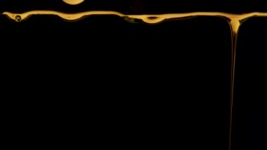 Siyah stüdyo arka planında altın bal damlaları. Kalın, tatlı sıvı damlıyor. Şeffaf renkli şurup ya da yağ damlacıkları. Kapatın. Yavaş çekim.