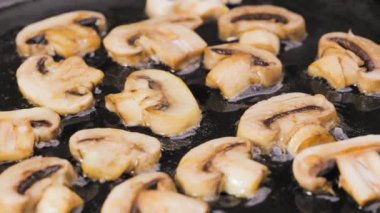 Dilimlenmiş şampiyon mantarları yakın planda sıcak tavada kızartılır. Şampiyonların altın dilimleri zeytinyağında kızartılır. Restoran için güzel bir duvar kâğıdı. Yavaş çekim.