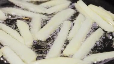 Yakından yağlı bir tavaya patates şeritleri dökerek. Patates kızartması Patates parçaları kızgın yağda kızartılır. Şişko sağlıksız fast food. Restoran için güzel bir duvar kâğıdı. Yavaş çekim.