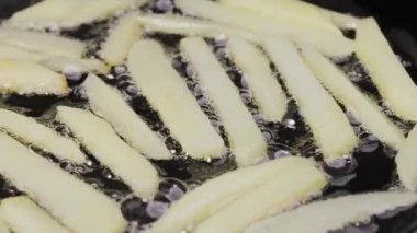 Yakından yağlı bir tavaya patates şeritleri dökerek. Patates kızartması Patates parçaları kızgın yağda kızartılır. Şişko sağlıksız fast food. Restoran için güzel bir duvar kâğıdı. Yavaş çekim.