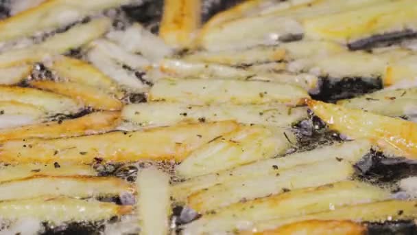 Cuñas crujientes doradas de papas se fríen en aceite en una sartén caliente en la cocina. El proceso de cocción de un plato de patata cerrar. Hermoso fondo de pantalla de cocina para restaurante. Movimiento lento. — Vídeo de stock