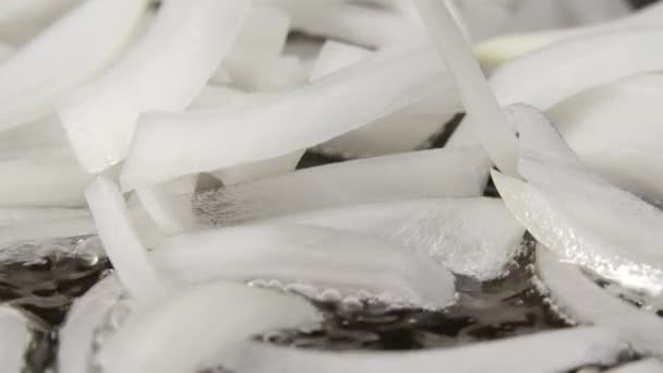 Sliced white onions are frying into a hot pan with oil. Macro shot of cooking fried onions in a frying pan. Preparing vegetables for cooking dinner. Close up. Slow motion. — Stock Video