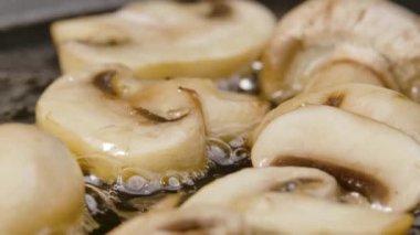 Kızartma tavasında zeytinyağında kızarmış şampiyon mantarı pişirme işlemi, yakın çekim. Makro atış. Aşçı sebze yağında mantar kızartıyordu. Pişirmek için kızartma tavasına. Yavaş çekim.