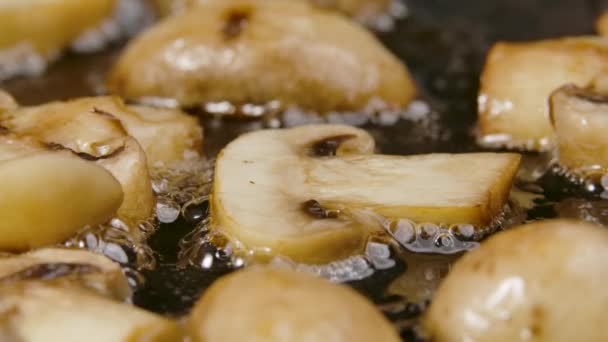 Τα ψιλοκομμένα μανιτάρια champignon τηγανίζονται σε ένα καυτό τηγάνι σε κοντινό πλάνο. Χρυσές φέτες από champignons τηγανίζονται σε ελαιόλαδο. Όμορφη ταπετσαρία του μαγειρέματος για εστιατόριο. Αργή κίνηση. — Αρχείο Βίντεο