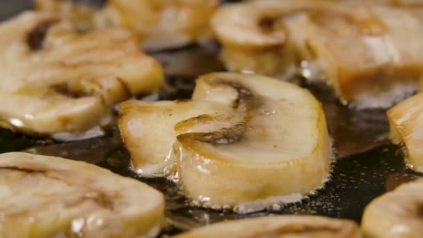 Os cogumelos de champignon fatiados fritam-se em uma panela quente no fim. As partes de ouro de champinhons fritam-se no óleo de azeitona. Papel de parede bonito de cozinhar para restaurante. Movimento lento. — Vídeo de Stock
