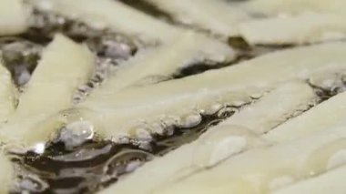Yakından yağlı bir tavaya patates şeritleri dökerek. Patates kızartması Patates parçaları kızgın yağda kızartılır. Şişko sağlıksız fast food. Restoran için güzel bir duvar kâğıdı. Yavaş çekim.