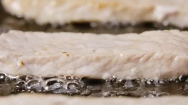 Tavuk fileto şeritleri sıcak tavada yağda kızartılır. Sulu hindi parçaları kızarmış. Sulu, sağlıklı et yemeği pişirirken yakın çekim. Restoran için güzel bir duvar kâğıdı. Yavaş çekim.