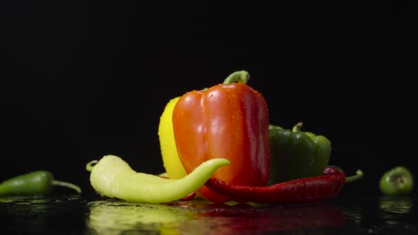 Peppers wet with drops of moisture on black background. Red, green and yellow hot chili, jalapeno and bell peppers are spinning covered with water droplets. Close up. Slow motion ready, 4K at 59.94fps — Stock Video