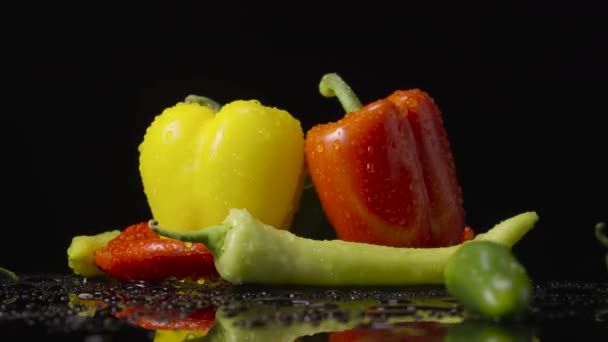 Pimientos mojados con gotas de humedad sobre fondo negro. El chile picante rojo, verde y amarillo, jalapeño y pimientos están girando cubiertos con gotas de agua. De cerca. Cámara lenta lista, 4K a 59.94fps — Vídeo de stock