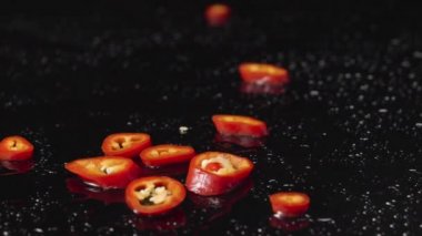 Islak siyah yüzeye düşen kırmızı acı biber dilimleri. Baharatlı sebze parçaları, acı yemek için bir malzeme. Restoran için vejetaryen yemek duvar kağıdı. Kapatın. Yavaş çekim.
