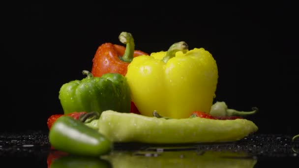 Rode, groene en gele hete chili, jalapeno en paprika 's draaien onder de douche. Rijpe groenten met water spatten roteren op zwarte studioachtergrond. Sluit maar af. Slow motion klaar, 4K bij 59,94fps — Stockvideo