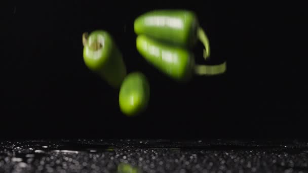 Los chiles jalapeños picantes verdes que golpean una superficie húmeda rebotan hacia arriba y forman un aerosol contra un fondo de estudio negro. Fondos de pantalla vegetal maduro picante para cocinar o restaurante. De cerca. Movimiento lento. — Vídeo de stock