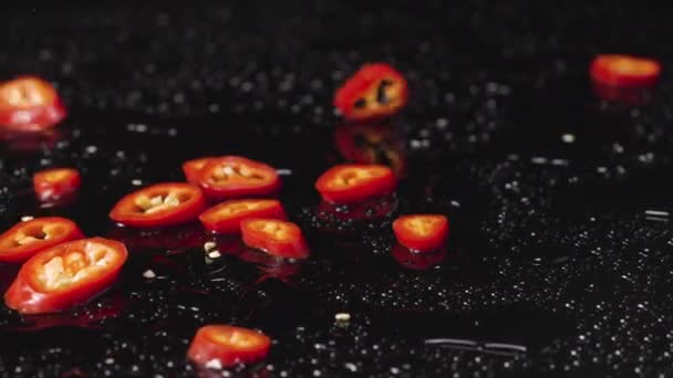 Tranches de piment rouge tombant sur une surface noire humide. Des morceaux de légumes épicés, un ingrédient pour un plat amer. Cuisine végétalienne papier peint pour le restaurant. Ferme là. Mouvement lent. — Video