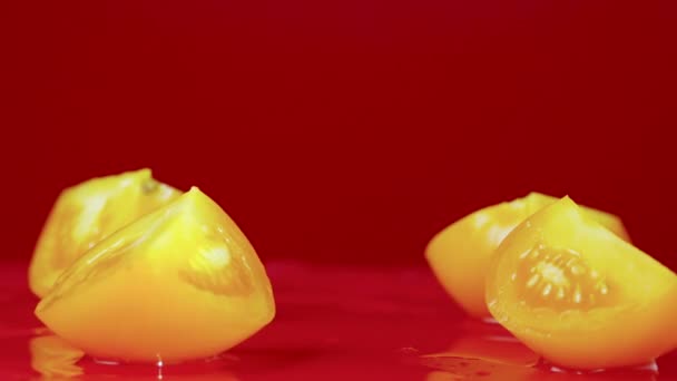 ビデオショットのセット熟した黄色のトマトスライスは、ぬれた反射テーブルの表面に落ちます。トマトスライスを閉じ、赤いスタジオの背景にスプラッシュで叩いてください。トマトが落ちると遅い動きで分割 — ストック動画