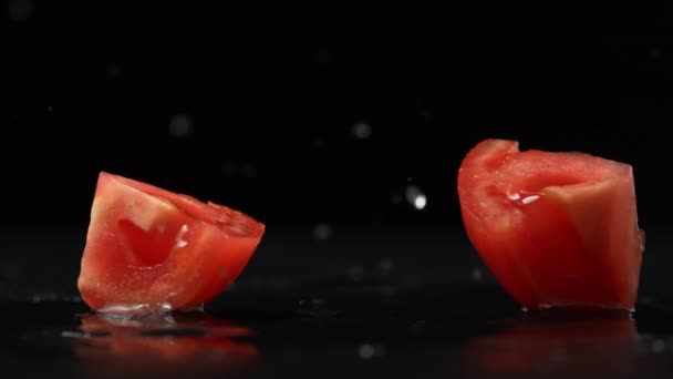 Närbild slow motion film av färsk röd tomat faller på våt yta och dela i två skivor. Skiva av tomat faller sönder på svart studio bakgrund. — Stockvideo