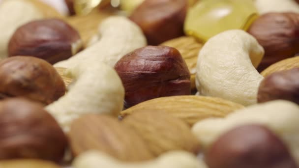 Aliran madu emas mengalir dan amplop campuran almond, kacang mete dan hazelnut dalam gerakan lambat. Kernel ditutupi dengan nektar tebal manis. Tutup rincian tembakan kacang dalam sirup manis. — Stok Video