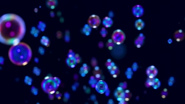 Розмиті кадри красивих блакитних веселкових мильних бульбашок, що летять у повітрі на чорному тлі. Багато бульбашок летять у космосі і мерехтять у світлі. Близько. Повільний рух . — стокове відео