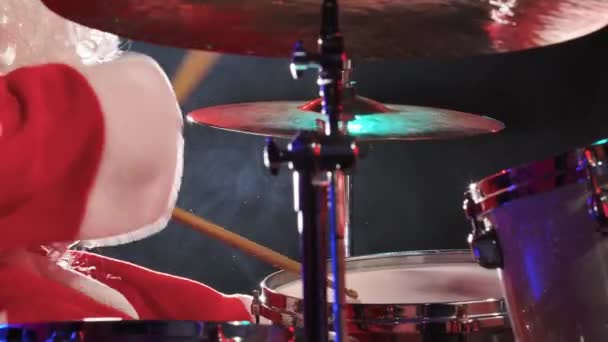 Zijaanzicht van de Kerstman in een rood kostuum met baard speelt de drums in een donkere studio met felle lichten. Een man in een carnaval kostuum voert een show uit op een nieuwjaarsfeest. Sluit maar af. Langzame beweging. — Stockvideo