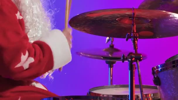 Side view of Santa Claus in a red costume with beard plays the drums in a dark studio with purple lights. A man in a carnival costume performs a show at a New Years party. Close up. Slow motion. — Stock Video