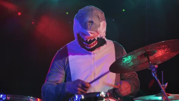 Музыкант в праздничном костюме акулы играет на барабанах и бьет по ударным тарелкам. Музыкант играет на праздничном концерте в темноте с ярким светом и дымом. Закрывай. Медленное движение. — стоковое видео