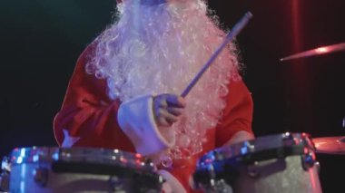 Noel Baba 'nın şenlikli performansı. Yeni yıl kostümü giymiş sakallı bir adam davul setini canlı çalıyor, aktif olarak davul ve perküsyon zillerini sopasıyla vuruyor. Kapatın. Yavaş çekim.