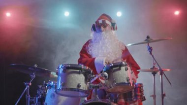 Kırmızı sakallı ve komik gözlüklü Noel Baba parlak ışıklar ve dumanla karanlık bir stüdyoda davul çalıyor. Karnaval kostümü giymiş bir adam yeni yıl partisinde gösteri yapıyor. Yavaş çekim.