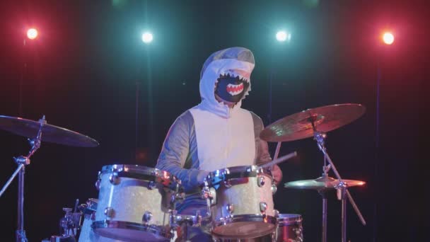 Mužský hudebník převlečený za žraloka hraje na bicí soupravu v tmavém studiu s jasnými barevnými světly. Slavnostní představení na zábavném večírku. Vánoce, nový rok, dobrá nálada. Zpomalený pohyb. — Stock video