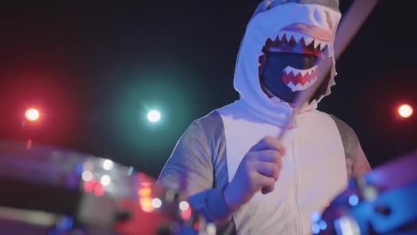 En manlig musiker förklädd till haj spelar trumset i en mörk studio med starkt färgat ljus. En festlig föreställning på en rolig fest. Jul, nyår, gott humör. Sakta i backarna. Närbild. — Stockvideo