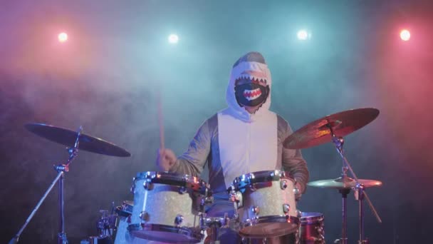 Музикант у святковому костюмі акули грає на барабанах і влучає в ударні цимбали. Музикант грає на святковому концерті в темряві з яскравими вогнями і димом. Повільний рух . — стокове відео