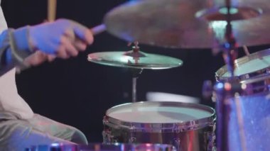 Festivalci köpekbalığı kostümlü müzisyenin yan görüntüsü davul çalıyor ve perküsyon zillerini vuruyor. Bir müzisyen karanlıkta parlak ışıklar ve dumanla bir festival konserinde çalar. Kapatın. Yavaş çekim.