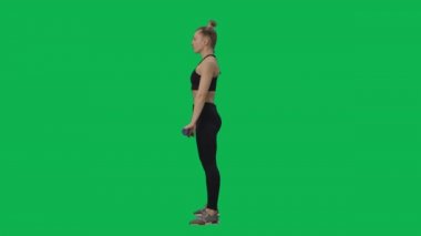 Genç bir kadın egzersiz yapıyor, barla çömeliyor. Kollar ve bacaklar için egzersiz, kadınlar için spor. Evde online eğitim. Yeşil ekran arka planında tam boy kenar görünümü. Yavaş çekim hazır 59.94fps.