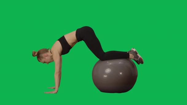 Young woman in sportswear performs twisting on fitness ball. Workout for arms, back muscles and abdomen, fitness for women. Side view full length on green screen background. Slow motion ready 59.94fps — Stock Video