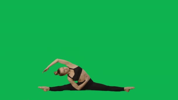 Junge Frau in Sportkleidung macht Yoga und dehnt den Körper. Workout, Fitness für Frauen, Aerobic. Seitenansicht in voller Länge auf grünem Hintergrund. Zeitlupe bereit 59.94fps. — Stockvideo