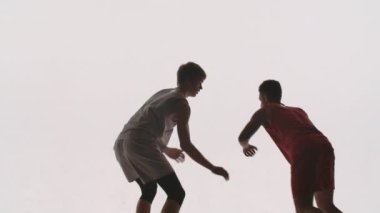 İki basketbolcu antrenmanda topla atış talimi yapıyor. Top yakalayan ve top sürüp sonra geri atan atletlerin silueti. Beyaz bir stüdyoda ağır çekimde çekildi..
