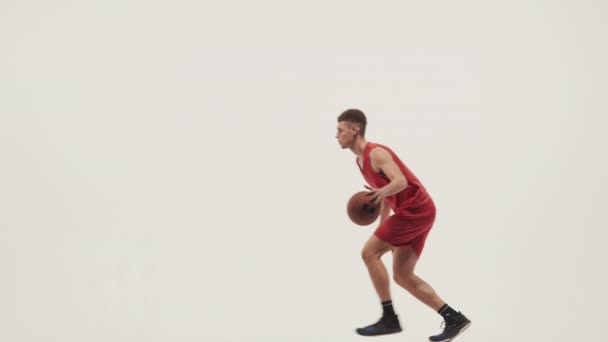 Spor üniformalı genç basketbolcu beyaz bir stüdyoda koşuyor ve salyalarını akıtıyor. Sporcu antrenman müsabakasına hazırlanıyor. Yavaş çekim. — Stok video