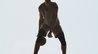 Spor giyimli basketbolcunun silueti beyaz stüdyo arka planında top sürme becerileri geliştiriyor. Profesyonel oyuncu basketbol yarışmasından önce antrenman yapar. Kapatın. Yavaş çekim hazır 59.94fps