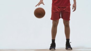 Spor giyimli basketbolcunun silueti beyaz stüdyo arka planında top sürme becerileri geliştiriyor. Profesyonel oyuncu basketbol yarışmasından önce antrenman yapar. Kapatın. Yavaş çekim hazır 59.94fps