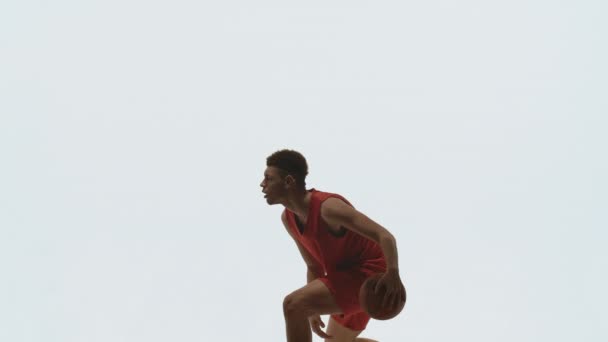 Chico jugador de baloncesto driblando pelota, golpeando en el suelo y lanza en la cesta. Atleta joven entrena antes de la competencia de streetball. Imagen tomada en el estudio sobre fondo blanco en cámara lenta. — Vídeos de Stock